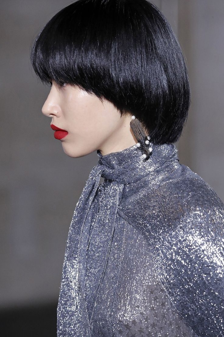 a woman with short black hair, wearing a silver sequin dress and red lipstick, poses for a close up portrait while looking away.
