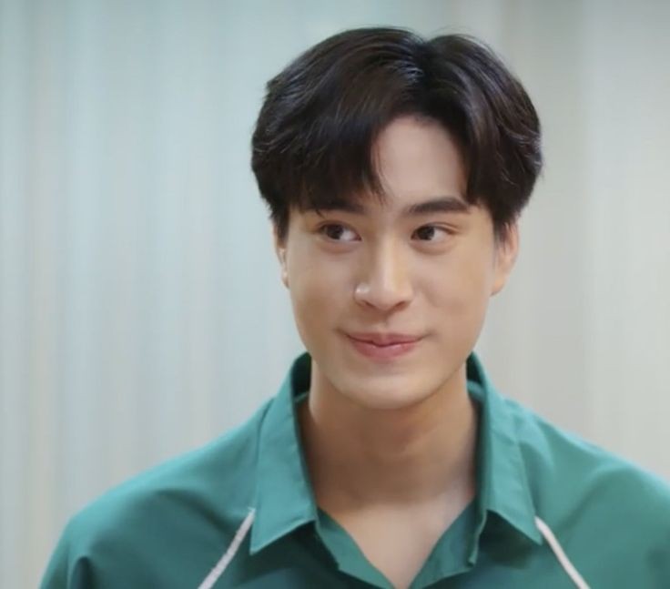 a headshot of a young asian man with short, black hair. he is wearing a green collared shirt and is smiling slightly, looking off to the left of the frame. the background is a soft white/grey color, suggesting an indoor setting.  the image is welllit with soft lighting, creating a warm and approachable feeling.
