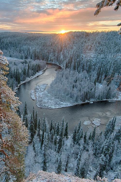 a stunning aerial view captures a snowy winter landscape at sunset. a river winds through a snowcovered forest of trees, with a vibrant sunset illuminating the sky. the scene is a picturesque display of nature's beauty in winter.