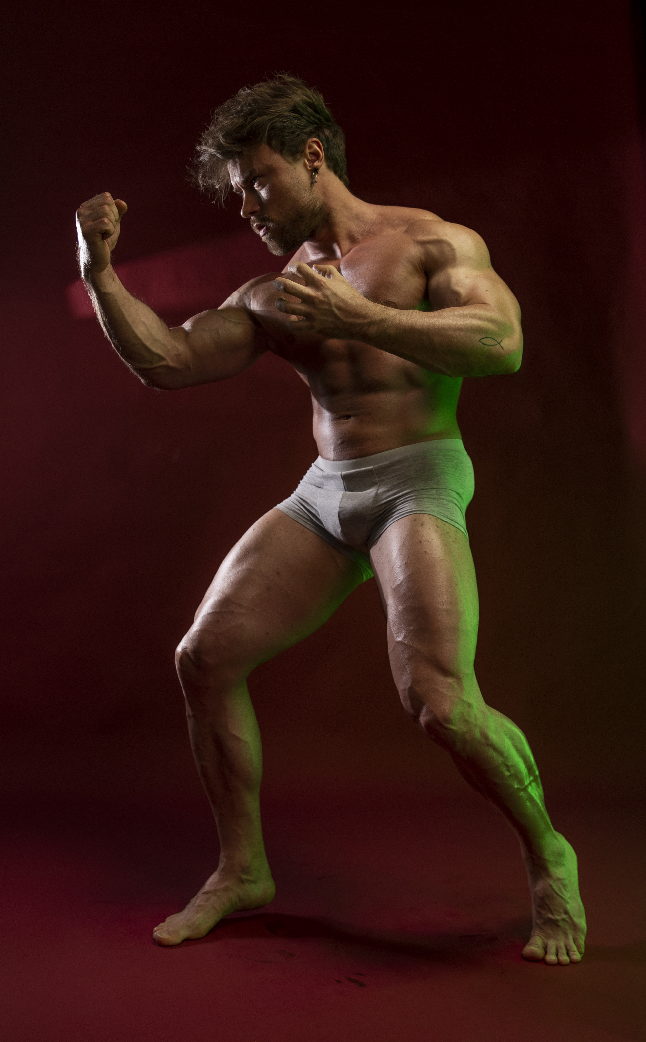 a muscular man is posing in a boxing stance, wearing only gray underwear. he is barechested and exhibits visible veins. the image appears to be a studio shot.