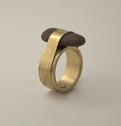 a closeup of a unique gold ring with a brown stone attached to it. the ring is made of a thin band of gold that wraps around the stone, and the stone is positioned horizontally on top of the band. the ring is set against a white background. the image is minimalist and modern, showcasing the beauty of the design.