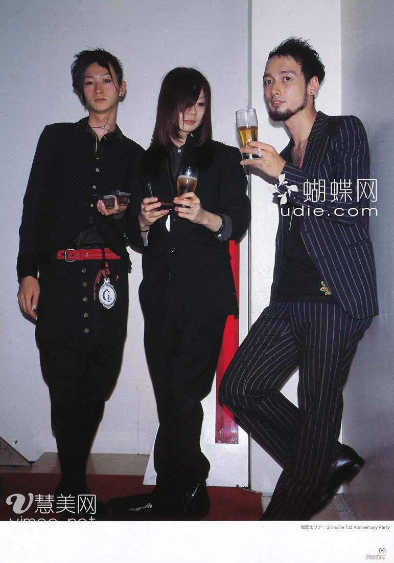 a photograph of three young men posing for the camera. they are all dressed in dark, stylish clothing which is typical of the visual kei japanese rock music scene. two of them are holding beers. the background is white and red, and the image appears to have been taken at a party.