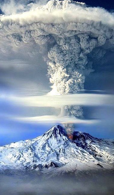 an aerial view of a volcanic eruption, with a massive ash cloud billowing into the sky. the snowcapped mountain is in the foreground, and the smoke is rising up towards the clouds. the eruption is very dramatic, with a lot of smoke and ash in the air. the mountain is covered in snow and ice, which contrasts with the dark grey ash cloud. this is a breathtaking image of nature's power, and it shows the beauty and danger that volcanoes can bring.