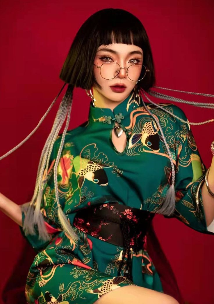 a young woman with black bobbed hair and bangs, wearing round glasses, poses for a portrait while wearing a green kimono with gold accents. she has a beautiful, delicate appearance, and her dark makeup accentuates her eyes.  she is styled to look elegantly trendy.