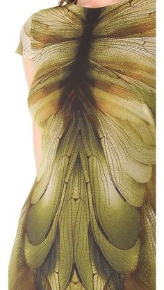 a closeup of a woman wearing a green and brown dragonfly wing pattern dress. the dress is very detailed and intricate, with delicate lines and patterns. the woman's skin is also visible, and she is wearing a simple necklace. the image is very elegant and stylish.