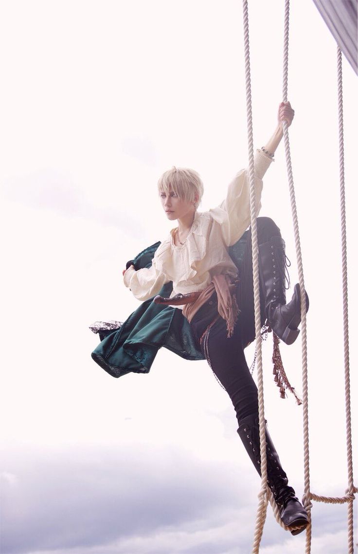 a person in a pirate cosplay, with white hair, a green jacket, and black pants, is swinging on a rope against a cloudy sky. they're wearing black boots. the image captures a moment of movement and adventure.