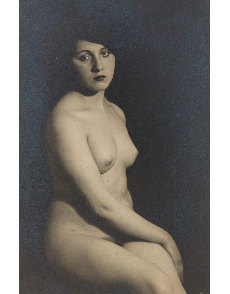a black and white, possibly sepiatoned, vintage photograph depicts a nude woman seated against a dark backdrop. the woman is positioned slightly angled to the viewer, her gaze directed forward with a pensive or melancholic expression. her body is subtly sculpted by the light and shadow. the image's style evokes classic portraiture of the early 20th century, suggesting a possible art deco influence.  the photograph is elegantly composed and utilizes the contrast between the dark background and the lighter tones of the woman's body to create a strong visual impact.