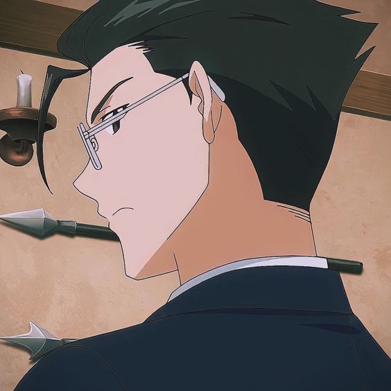 the image shows a closeup profile view of a young man from an anime. he has dark hair swept back from his forehead, fair skin, and wears thinframed glasses. his expression is serious and contemplative. he wears a dark suit jacket, suggesting a formal or professional setting. the background is a muted tan color, hinting at a simple indoor environment. the overall tone of the image is subdued and mysterious, emphasizing the character's intense gaze.
