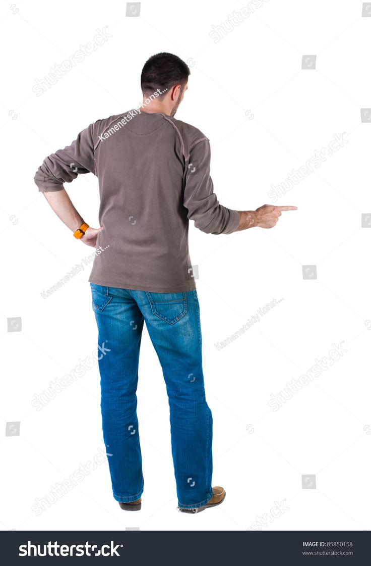 a young man is standing with his back to the camera, wearing jeans and a brown tshirt. he is pointing with his right hand to the side. the background is white.