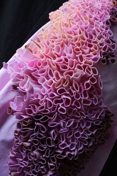 a closeup shot of a beautiful fabric ruffle. the ruffle is made of a delicate pink fabric that has been folded and stitched to create a flowing, delicate texture. the ruffle is ombrecolored, with a lighter pink at the top and a deeper purple at the bottom. the fabric is very soft and smooth to the touch, and it appears to be quite sheer. the photo is taken in a way that highlights the intricate details of the ruffle, making it appear elegant and romantic.