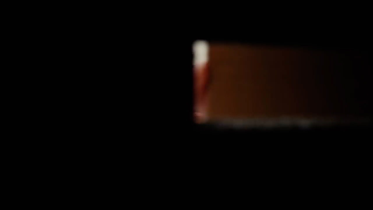 a blurredout image showing the spine of a book against a black background. only the spine and a sliver of the pages are visible. the spine is a rich brown color with a hint of red, and the pages are a creamy white. the image is dark and mysterious, with the book as the only source of light.