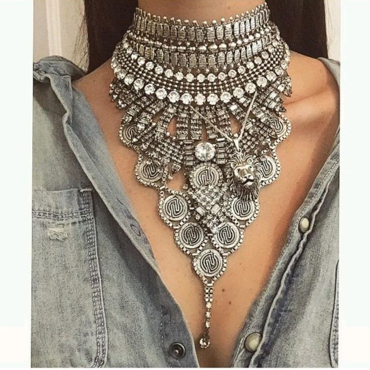 a woman wearing a large silver statement necklace. it is made up of multiple chains and charms, and hangs down to her chest. the necklace is very ornate and eyecatching, and it is a great example of bohochic style.