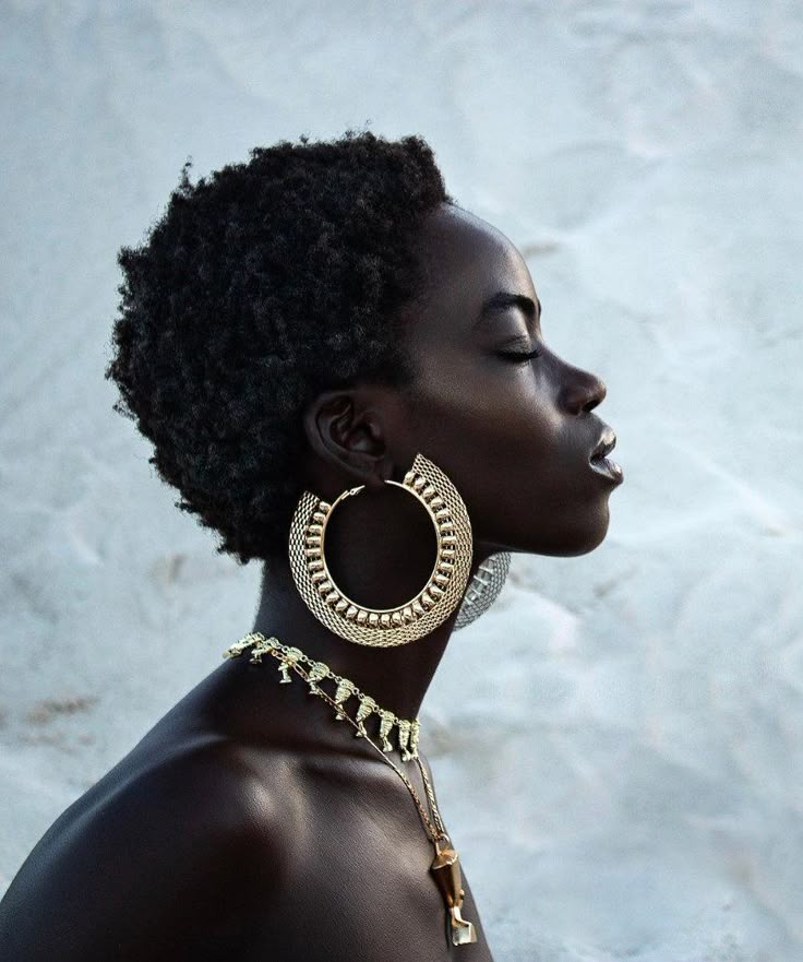 a portrait of a beautiful black woman with short afro hair, wearing large gold hoop earrings and a layered gold necklace. her eyes are closed, and she is shown in a side profile. the focus is on her jewelry, skin tone, and hairstyle.