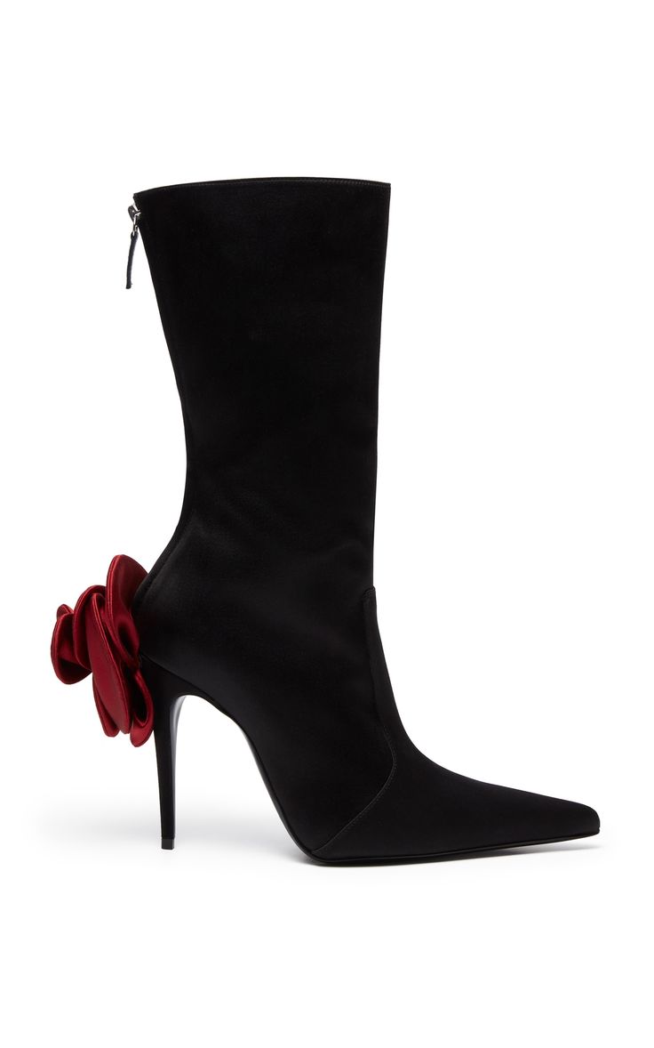 a pair of elegant black satin ankle boots with a pointed toe and a red satin bow detail on the side.  the boots are shown on a white background in a studio shot.  the heels are high and stilettoshaped.  a side zipper is visible.