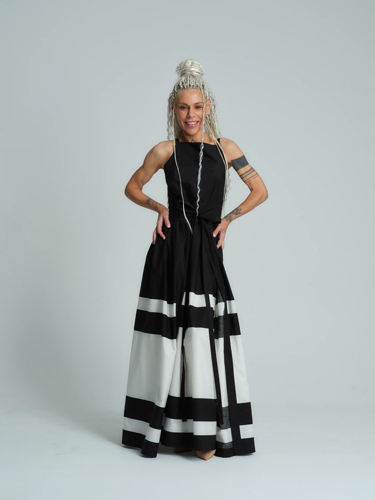 a woman in a black and white striped dress is posing in a studio setting. she has blonde hair and is smiling. she looks elegant and stylish. the background is a plain white wall.