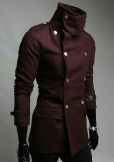 a man is wearing a stylish maroon doublebreasted coat. the coat has a high standup collar with a gold button. he has a gold button on each side of the front of the coat and a gold button down each of the two lines of buttons. his sleeves are rolled up to his elbows. he is wearing a watch on his left wrist. the man looks very fashionable in the coat.