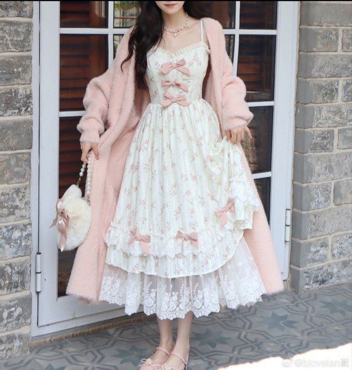 young woman is posing indoors wearing a delicate and feminine outfit. she is wearing a white dress with pink floral print, lace trim, and bows. the dress has a tiered skirt and is paired with a pink fluffy cardigan. she is also wearing pink shoes and carrying a fluffy pink purse. the photo is welllit and the woman is the central focus. the overall aesthetic is romantic and dreamy.
