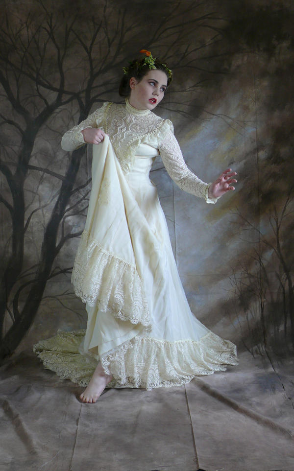 the image is a portrait of a woman wearing a beautiful antiquestyle, ivory wedding dress. the dress features intricate lace details, ruffles, and long sleeves. she is barefoot and has a floral crown in her hair. the background is a dark, painterly depiction of a forest with bare, gnarled trees.  the overall mood is ethereal, mysterious, and slightly haunting. the lighting and posing contribute to a romantic and dreamlike atmosphere. the woman's expression appears pensive or slightly fearful, adding to the image's intrigue. the high quality of the photography suggests a studio setting with careful attention to detail.