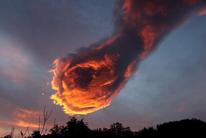 a vibrant sunset sky is painted with dramatic clouds. the orange and red hues of the setting sun illuminate the clouds, creating a fiery and glowing spectacle. the clouds appear as if they are a hand reaching up towards the heavens.