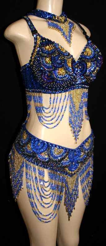 a blue and gold sequined and beaded belly dance costume is displayed on a mannequin. the costume consists of a halter top bra, a belt, and a necklace. the bra and belt are adorned with intricate sequin and beadwork patterns and feature beaded fringe. the mannequin is set against a black background.