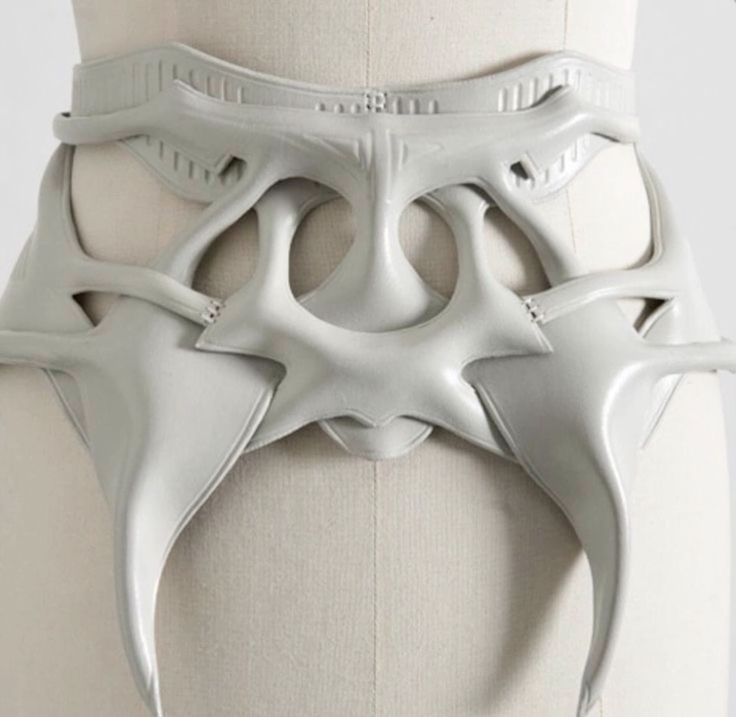the image shows a closeup view of a white leather belt with a complex, sculptural design. the belt is cinched at the waist of a mannequin, and its organic, bonelike forms extend outwards from the center.  the lighting is soft and diffused, highlighting the smooth texture of the leather.
