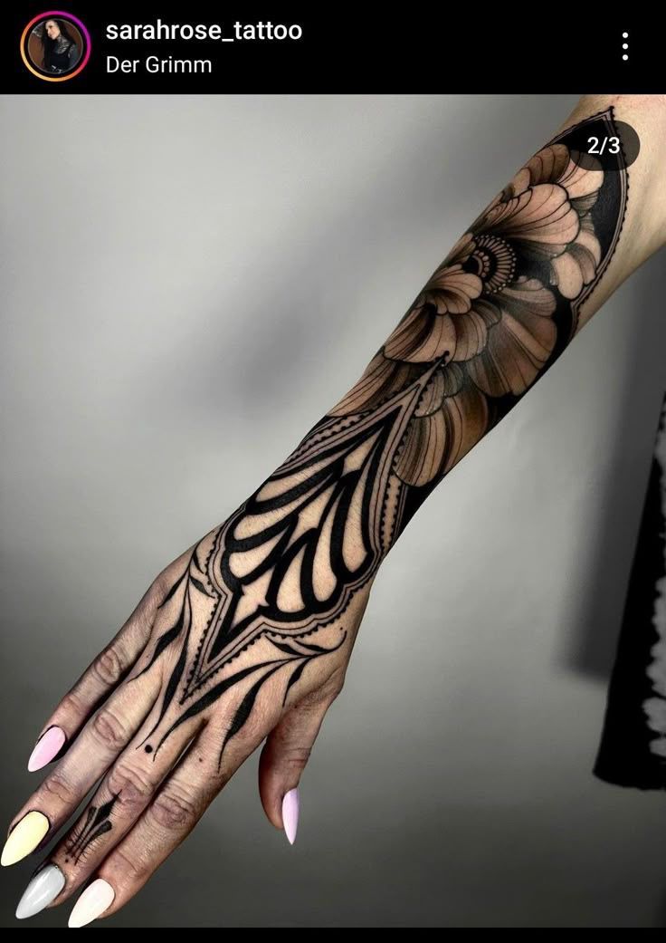 the image shows a person's arm with a full sleeve tattoo. the tattoo is primarily black and white, featuring an intricate floral design that extends from the upper arm down to the hand. the design incorporates various shapes and patterns, creating a visually striking and detailed piece of body art. the person has manicured nails with different colors of nail polish.