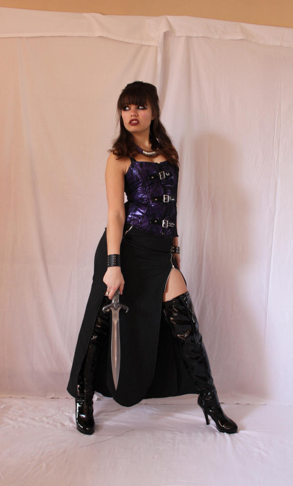 a fulllength shot of a young woman posing in a studio against a white background. she is wearing a purple corset, a long black skirt with a slit, and black thighhigh boots. she is holding a sword. she has dark brown hair with bangs and is wearing dark makeup.  she appears confident and powerful. the overall style is gothic or fantasyinspired.