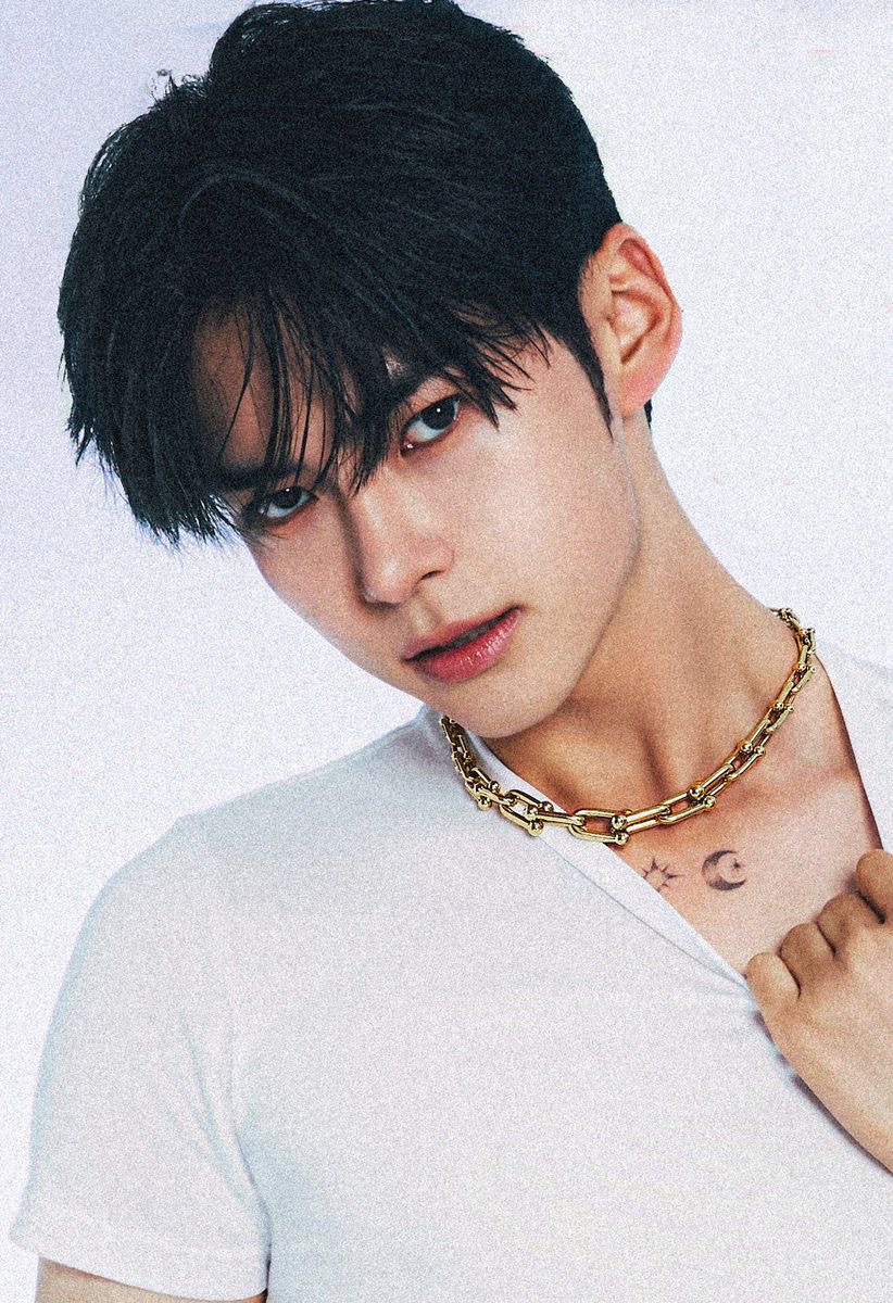 a closeup portrait of cha eunwoo, a member of the kpop group astro. he is wearing a white tshirt and a gold chain. he has a tattoo of a crescent moon and stars on his chest. he is looking directly at the camera with a smoldering expression. the lighting is soft and flattering. the background is a plain white wall.