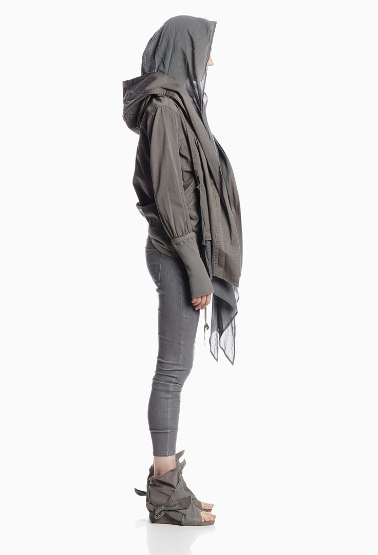 a woman wearing a gray hooded jacket and pants is standing with her side facing the camera in a studio with a white background. she is wearing unique gray footwear.