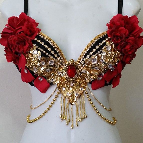 a black bra is heavily embellished with red flowers, gold beads, sequins, rhinestones, and gold chains. the center of the bra features a large red jewel surrounded by gold detailing.