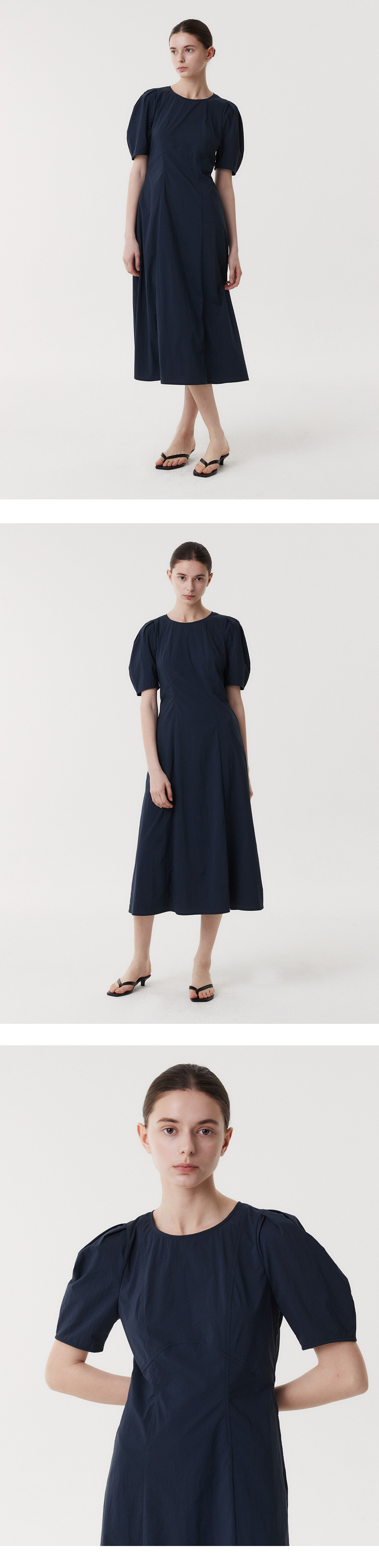 the image shows a woman wearing a navy blue midi dress with puff sleeves and sandals. the woman is standing in a white background. the dress is formfitting and has a simple design.