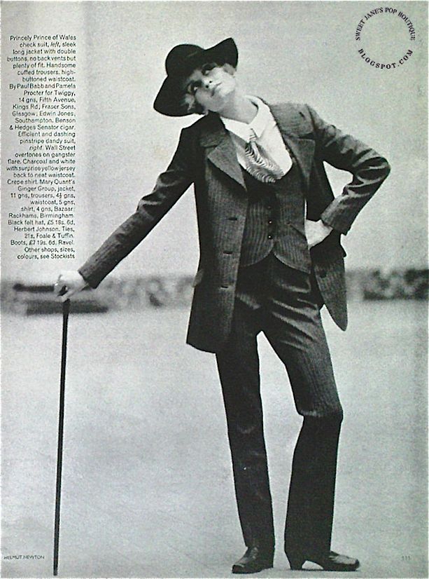 a black and white photo of a fashion model posing in a pinstripe suit with a black hat, holding a cane. she has a cigarette in her hand, and her clothes are styled in a 1960s, 70s way.