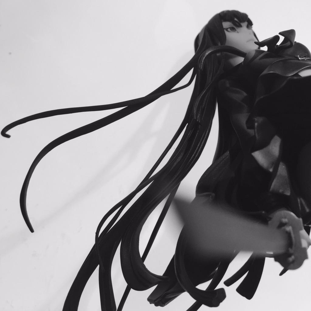 the image shows a black and white photo of an anime action figure with exceptionally long black hair. the figure is captured in motion, seemingly midattack, with her sword extended. the perspective is from a low angle, adding to the sense of power and movement.  the lighting is soft, creating smooth shadows and highlighting the details of the figure.