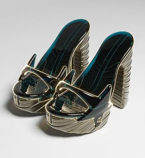 this image features a pair of futuristiclooking, highheeled sandals with a platform base. the shoes are made of a metallic material that appears to be gold or silver. the straps and upper portion of the shoes have a teal or blue color, creating a striking contrast with the metallic base. the sandals have a very abstract and geometric design, with intricate details and an overall shape that appears to be inspired by nature. they exude a sense of both elegance and futuristic sophistication, making them a bold and eyecatching fashion statement.