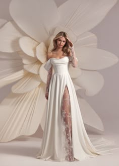 a bride wearing a white satin wedding dress with a lace overlay stands in a studio against a backdrop of white fabric. she poses with her hands on her hips, looking at the camera. the dress has a deep neckline and a thighhigh slit. the bride is elegant and beautiful.