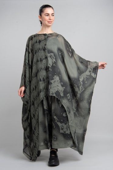 a woman stands in a studio wearing a dress. the dress has a unique print design. the woman is also wearing shoes.