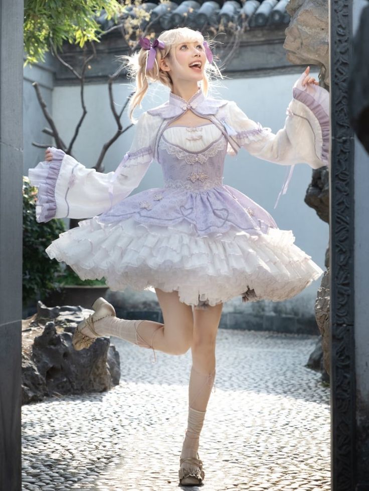 a young woman wearing a elaborate lavender and white lolita fashion dress  poses in a sunny traditional chinese garden.  she is smiling brightly and looks joyful.  her outfit is highly detailed with lace, ruffles, and bows. the garden setting features stonework and greenery.