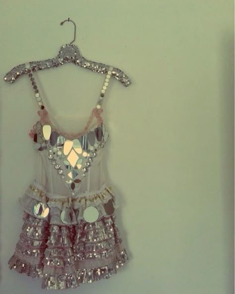 a pink and white party dress with mirror sequins is hanging on a hanger against a white wall.  the dress has a white corset bodice with mirror pieces, and a pink and white skirt that is made of layers of tulle and sequined fabric.