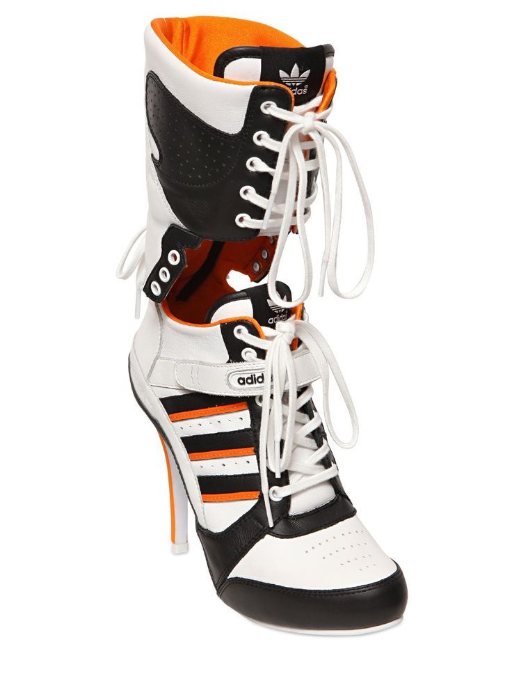 a pair of white adidas highheeled boots with black and orange accents. the boots have laces up the front and are made of a combination of leather and synthetic materials. the heels are stiletto style and the boots have a sporty look.