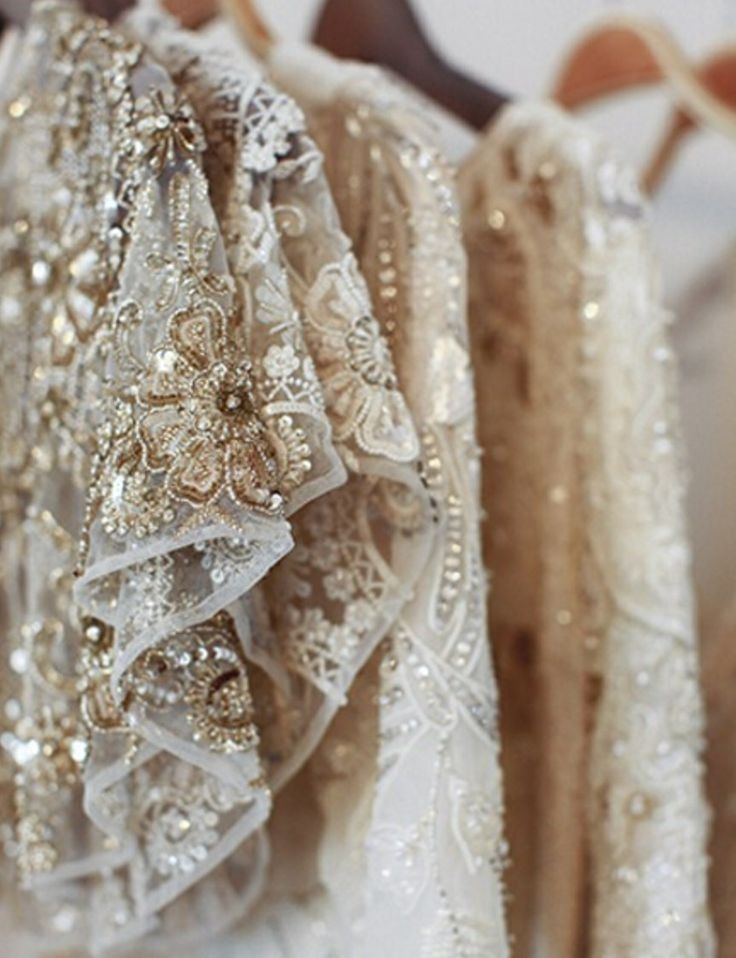 a closeup shot of several luxurious wedding dresses hanging on a rack. the dresses are predominantly ivory and champagne colored, featuring intricate lace, beaded embroidery, and sequins.  the fabrics appear delicate and the overall aesthetic is elegant and romantic. the image focuses on the rich textures and details of the dresses, highlighting the craftsmanship.