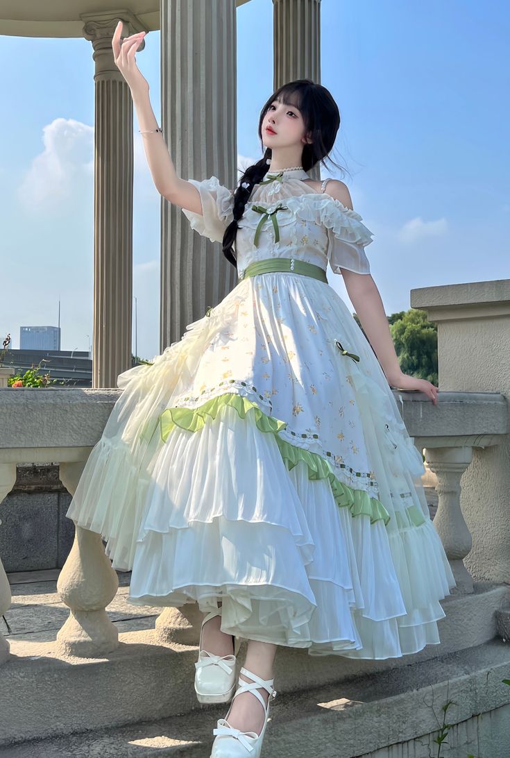 a young woman in a flowing white and green lolita dress poses on a balcony with white balustrades and towering columns. the dress features delicate floral embroidery, layers of ruffled tulle, and offshoulder sleeves.  she is elegantly posed, her arm gracefully raised, showcasing the dress's movement and her own poise. the natural sunlight illuminates the scene, creating a bright and airy atmosphere.