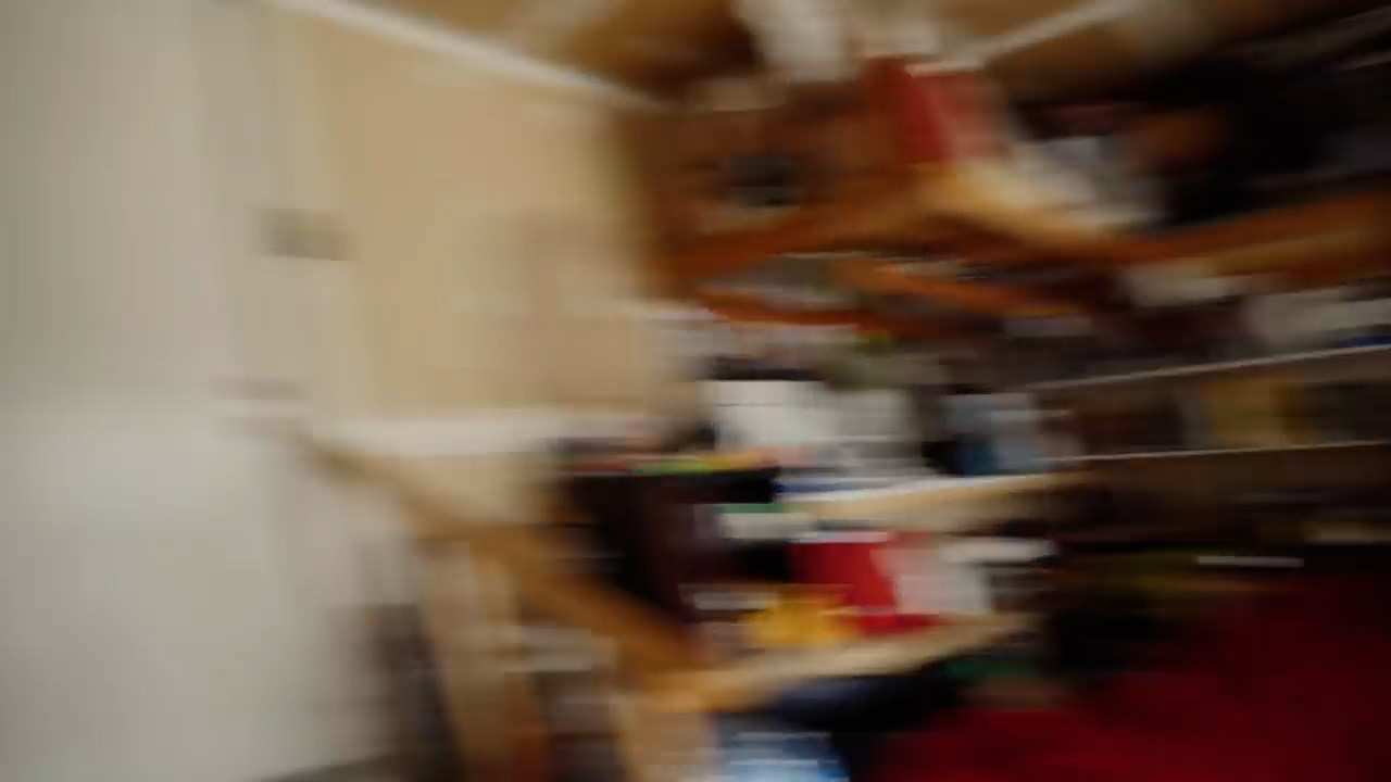 a blurry indoor photograph of a messy shelf and staircase. the walls are beige and the image is poorly lit.