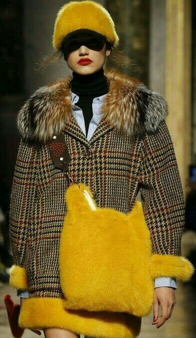a stylish woman in a yellow fur hat, a yellow fur handbag, and a black and yellow plaid coat. she's wearing sunglasses and red lipstick, and her look is chic and sophisticated.