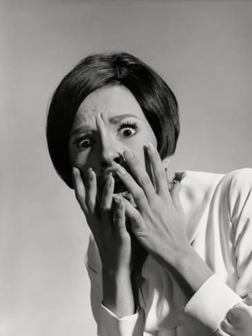 a woman in a black and white portrait is shown covering her face with both her hands. she looks extremely scared.  her lips are slightly parted, and her eyes are wide with fear.  she looks like she is about to cry.  the woman's hair is short and styled in a bob. her shirt is buttoned up to her collar. she appears to be in distress and is covering her face to block out the world.
