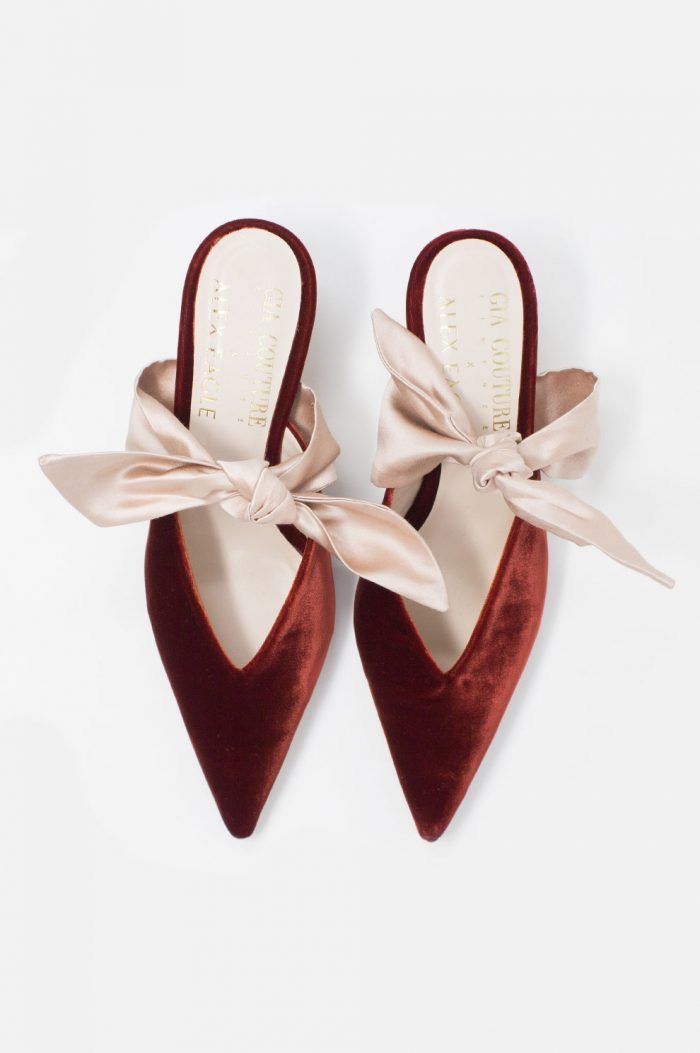 a pair of burgundy velvet pointedtoe mules are showcased against a white background. each shoe is adorned with a large, beige satin bow. the brand "gia couture" is printed on the insole of each shoe.