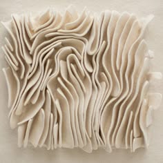 a closeup of a white, abstract sculpture made of textured, ruffled fabric or paper. the sculpture is arranged in a series of overlapping, curved shapes, creating a sense of depth and movement. the white color and simple form give the piece a minimalist aesthetic. it is a modern, contemporary art piece that could be used as a wall decoration.