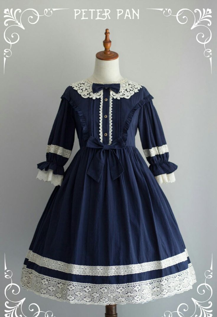a navy blue lolita dress with white lace trim and a peter pan collar is shown on a mannequin against a gray background. the dress has long sleeves, a full skirt, and a bow at the waist. the dress is very detailed and wellmade, and it would be perfect for a special occasion.