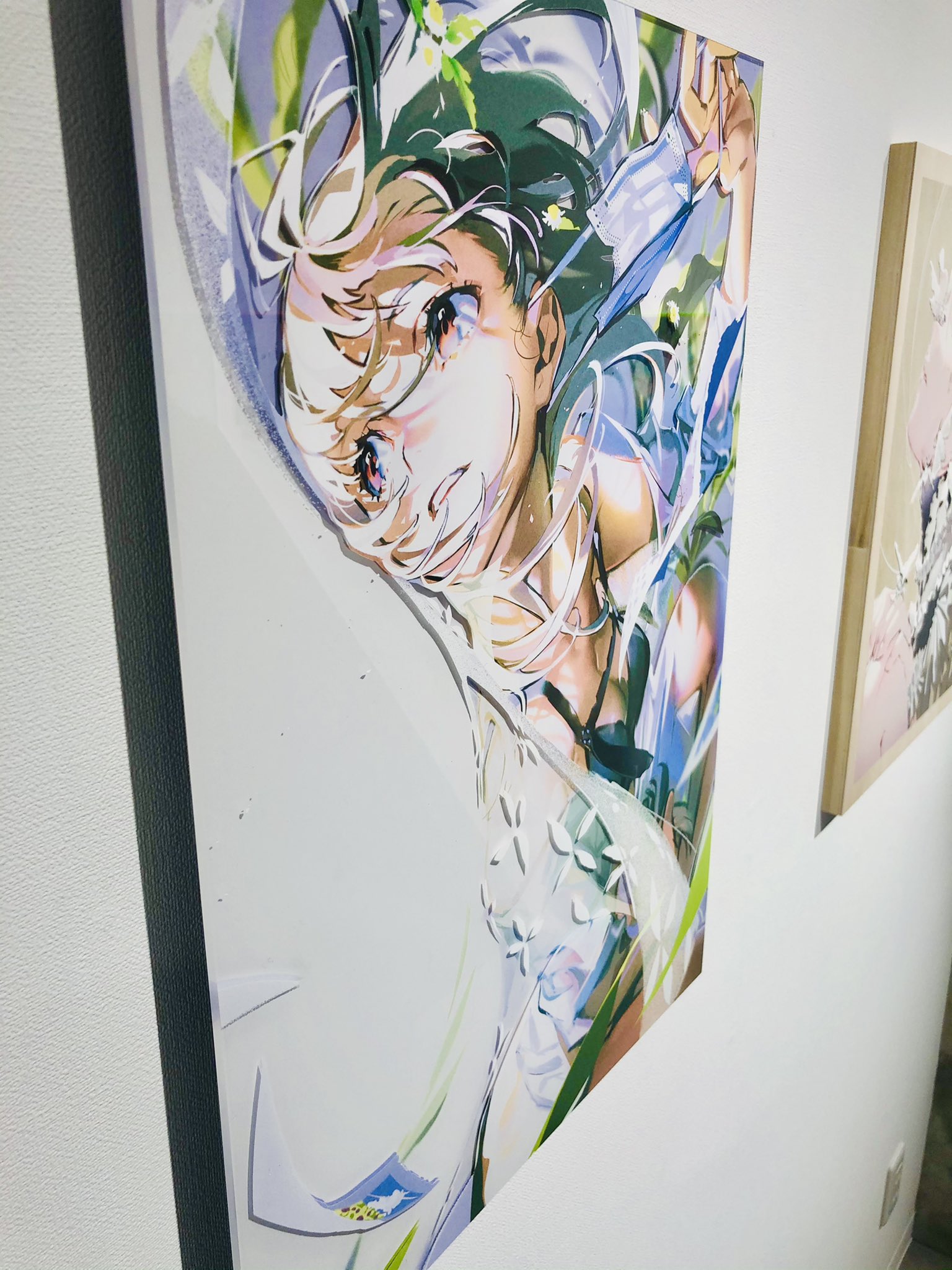 a large animestyle painting of a girl hangs on a white wall in a room, illuminated by natural light. the girl, with flowing hair and a whimsical expression, appears to be surrounded by nature, suggesting a vibrant and carefree scene.  the artwork's bright colors and dynamic composition add a touch of personality to the minimalist decor. to the right, a corner of a second painting is visible, hinting at a curated collection.