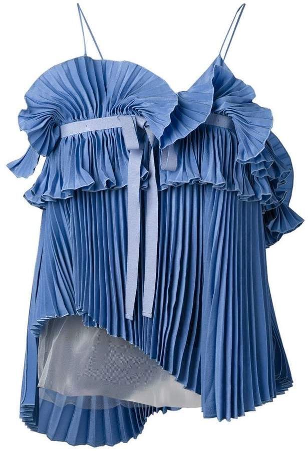 a sleeveless blue top made from pleated fabric with ruffled detailing around the upper part and held up by spaghetti straps. it features a ribbon accent and an asymmetrical hem with a visible lightercolored lining underneath.