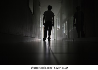 a silhouetted figure walks down a dark hallway with light at the end. another shadowy figure is visible on the right side of the hallway.